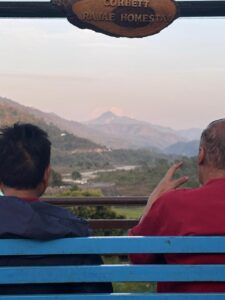 Two guests looking at the mountain view from a bench under the Rajae Homestay sign.