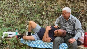 One senior man resting his head on his friend's lap outdoors.